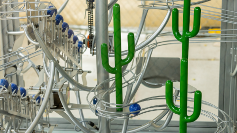 Blue golf balls roll down track behind miniature saguaros in a ball machine display.